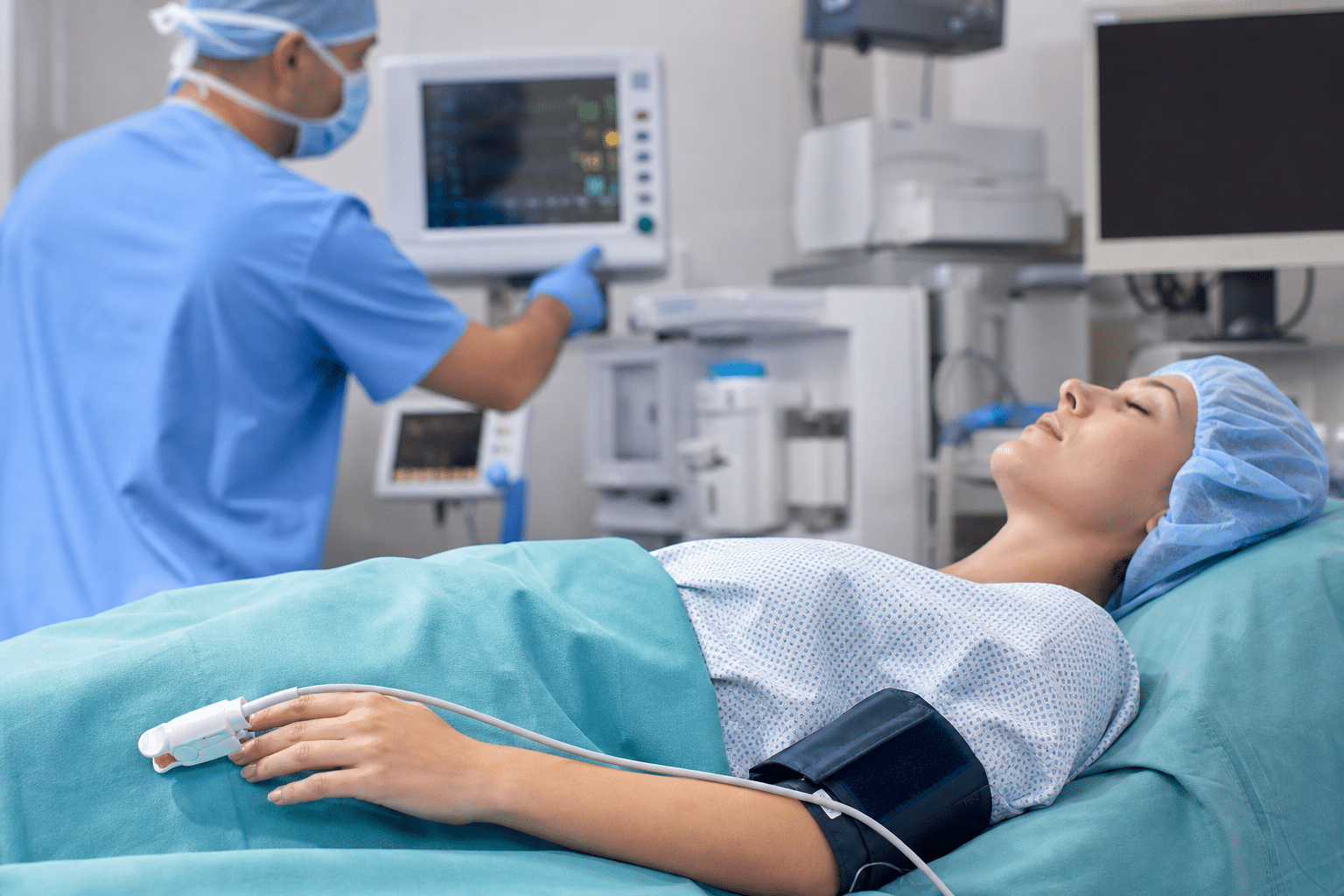Ein Patient liegt während einer Sedierung auf dem OP-Tisch und wird mit Pulsoximeter und Blutdruckmessgerät überwacht.